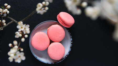Pink macaroon cookies and a branch of blooming cherry on a black background. Sweet dessert.の写真素材