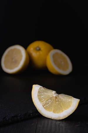 Slices of lemon and a whole yellow fruit lie on a black stone. Dark background.の写真素材