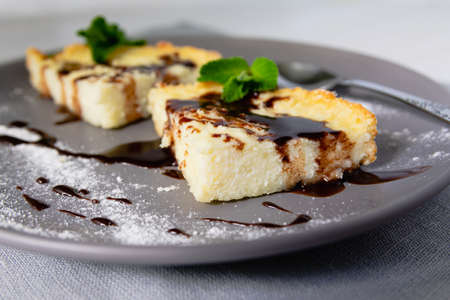 A serving of cheesecake in the form of triangular slices lies on a plate and is decorated with liquid chocolate closeup.の写真素材