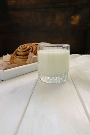 Yeast baked roll with cinnamon and a glass of milk on a white wooden background.の写真素材