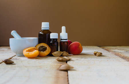 Apricot kernel cosmetic oil in dark glass bottles and a porcelain mortar on a light wooden table. Natural oilsの写真素材