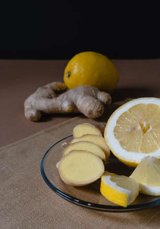 Slices of lemon and ginger lie on a plate on a brown background. Ingredients for making warming cold tea.の写真素材