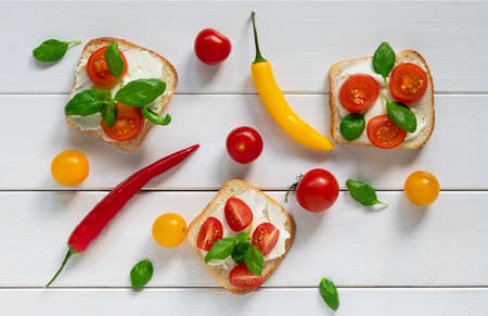 A layout of bruschetta with cheese and cherry and many multicolored tomatoes and peppers and basil leavesの写真素材