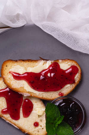 Two toasts with butter and blackcurrant jam decorated with mint leaves. The concept of a simple breakfast in a country house. The vertical orientation of the frame.の写真素材