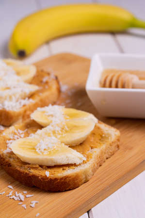 Sandwich with peanut butter, banana, coconut and honey in a bright kitchen. Traditional american breakfast. Vertical orientation.の写真素材