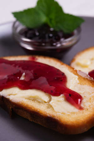 Toast with butter and blackcurrant jam decorated with mint leaves. The concept of a simple breakfast in a country house. The vertical orientation of the frame.の写真素材