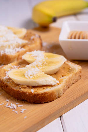 Sandwich with peanut butter, banana, coconut and honey in a bright kitchen. Traditional american breakfast. Vertical orientation.の写真素材