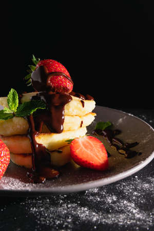 Cheesecakes or curd pancakes lie on a dark background with a pyramid and decorated with liquid chocolate and strawberries. Traditional Russian and Ukrainian dish.の写真素材