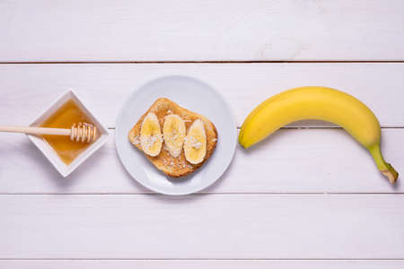 Crispy toast with peanut butter, banana slices, honey. Classic american breakfast on a white wooden background.T op viewの写真素材