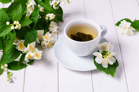 Green tea with jasmine in a white cup on a white wooden background and a branch of blooming jasmineの写真素材