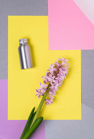 A bottle of rejuvenating herbal cosmetic serum lies next to a hyacinth flower against a background of colored blocks.の写真素材