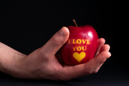 Ripe red apple with the inscription I love you in a mans hand on a dark background. Creative declaration of love.の写真素材