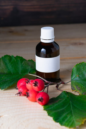 Glass bottle with tincture and ripe hawthorn berries on a wooden background.の写真素材
