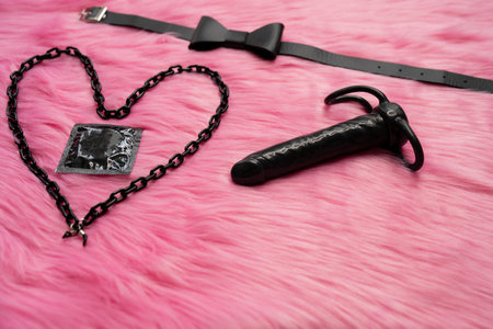Concept of safe sex and couple games.  Condom next to heart and butterfly tie and dark vibrator. Adult content of sex toysの写真素材