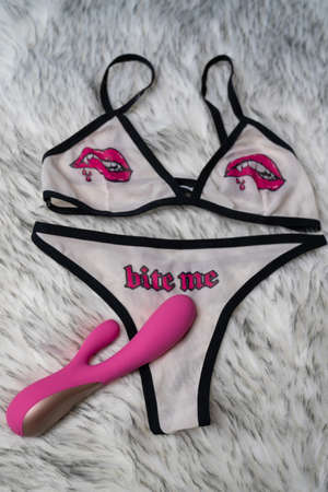 woman's sexy white underwear with lips and word "bite me" print, on the gray fur background. Pink vibrator dildo sex toy is on the pantiesの写真素材