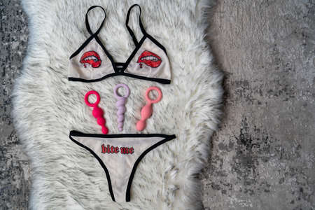 woman's sexy white underwear with lips and word "bite me" print, on the gray fur background. Different sex toys anal butt plugs are next to the panties. Bedroomの写真素材