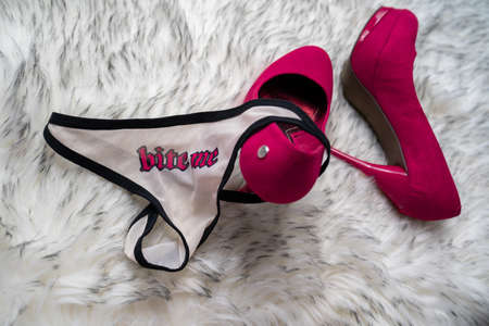 sexy red heels shoes near the white lingerie with lips and "bite me" prints, at the gray fur background in the bedroom. mistress concept and temptation.の写真素材