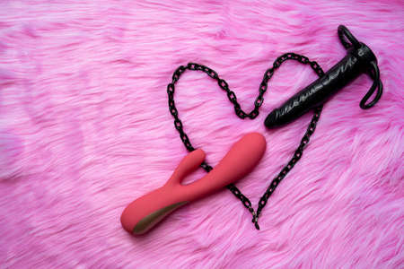 dark sex toy and pink vibrator ext to  heart, on the pink fur background of bedroom. Concept of heart and arrow romanceの写真素材