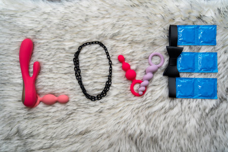 the word love made of sex toys and condoms on gray fur background, concept of seduction, introduction to couple game, i love you phraseの写真素材