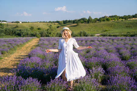 woman model in white dress outfit with hat is standing dancing in lavender field, photo session. Concept of freedom. Good picture for cover, calendar, postcard, wallpaperの写真素材