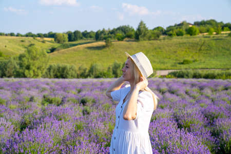 woman model in white dress outfit is standing in lavender field, photo session. Portrait of beautiful girl in hat. Good picture for cover, calendar, postcard, wallpaper, backgroundの写真素材