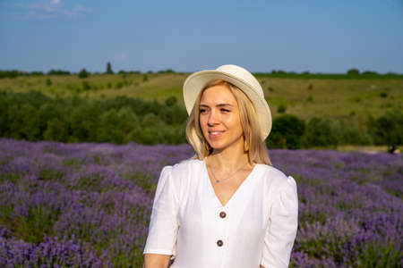 woman model in white dress outfit is standing in lavender field, photo session. Portrait of beautiful girl in hat. Good picture for cover, calendar, postcard, wallpaper, backgroundの写真素材