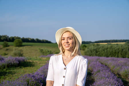 woman model in white dress outfit is standing in lavender field, photo session. Portrait of beautiful girl in hat. Good picture for cover, calendar, postcard, wallpaper, backgroundの写真素材