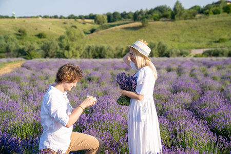 couple in white matching outfit in lavender field, photo session. man is proposing to woman with ring. engagement day. romance and true love in relationship. They are happy huggingの写真素材