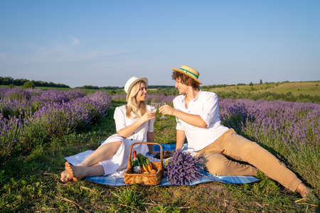 two persons couple in matching outfit have picnic in lavender field. They have fun, laugh and are feeding each other for photo session. Romantic relationship conceptの写真素材