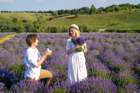 couple in white matching outfit in lavender field, photo session. man is proposing to woman with ring. engagement day. romance and true love in relationship. They are happy huggingの写真素材