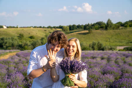 couple in white matching outfit in lavender field, photo session. man is proposing to woman with ring. engagement day. romance and true love in relationship. They are happy huggingの写真素材