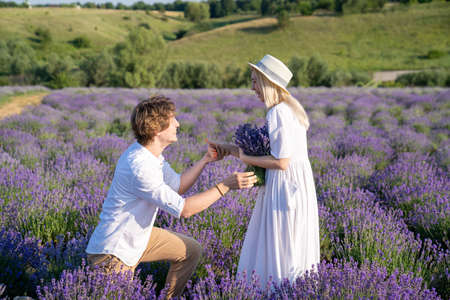 couple in white matching outfit in lavender field, photo session. man is proposing to woman with ring. engagement day. romance and true love in relationship. They are happy huggingの写真素材