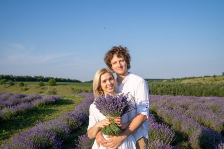 portrait of a couple in matching white outfit. Girl is holding lavender bouquet and smiling. They are happy and hug showing emotions. Good picture for cover, calendar, postcardの写真素材
