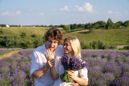 couple in white matching outfit in lavender field, photo session. man is proposing to woman with ring. engagement day. romance and true love in relationship. They are happy huggingの写真素材