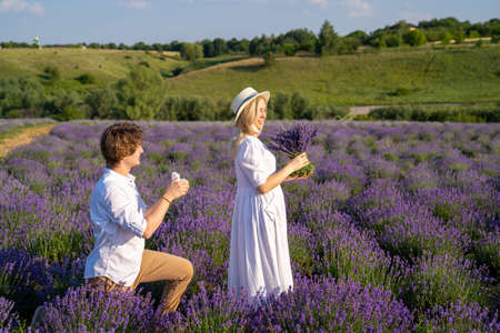 couple in white matching outfit in lavender field, photo session. man is proposing to woman with ring. engagement day. romance and true love in relationship. They are happy huggingの写真素材