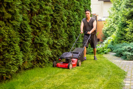 middle aged handsome man wearing home clothes is cutting the lawn, process to cut the grass at the...
