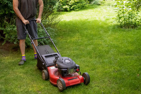 middle aged handsome man wearing home clothes is cutting the lawn, process to cut the grass at the...
