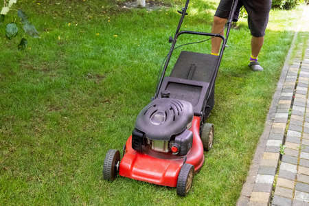 middle aged handsome man wearing home clothes is cutting the lawn, process to cut the grass at the...