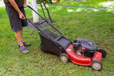 middle aged handsome man wearing home clothes is cutting the lawn, process to cut the grass at the...