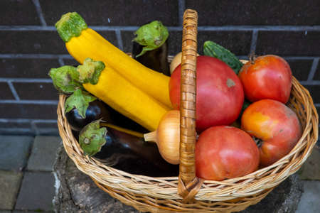 wicker wooden basket full of fresh ripe vegetables: tomato, cucumber, onion, zucchini, eggplant on brick background. Early harvest. Concept of healthy eating lifestyle dietの写真素材