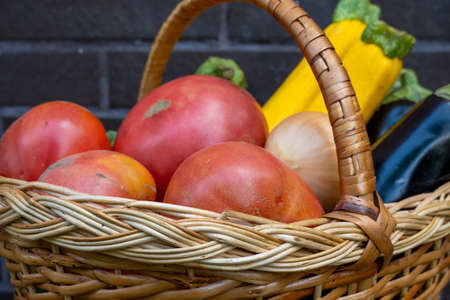 wicker wooden basket full of fresh ripe vegetables: tomato, cucumber, onion, zucchini, eggplant on brick background. Early harvest. Concept of healthy eating lifestyle dietの写真素材