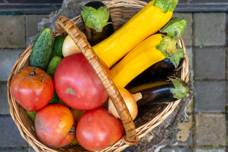 wicker wooden basket full of fresh ripe vegetables: tomato, cucumber, onion, zucchini, eggplant on brick background. Early harvest. Concept of healthy eating lifestyle dietの写真素材