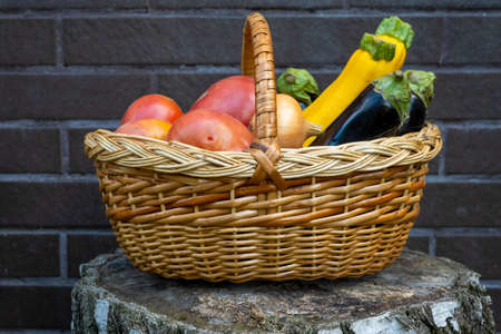 wicker wooden basket full of fresh ripe vegetables: tomato, cucumber, onion, zucchini, eggplant on brick background. Early harvest. Concept of healthy eating lifestyle dietの写真素材