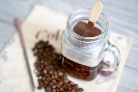 strong black coffee espresso shot in glass cup, coffee set on table, long spoon and coffee beans on...