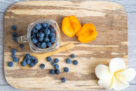blur background, top view on healthy, organic, gluten free breakfast served in transparent glass cup filled with blueberry and apricot on a wooden plate, near wooden spoon. Healthyの写真素材
