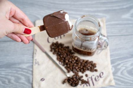 blur background, woman hand with manicure holds half eaten ice cream and pours it into strong black coffee espresso shot in glass cup, coffee set on table, long spoon and coffeeの写真素材