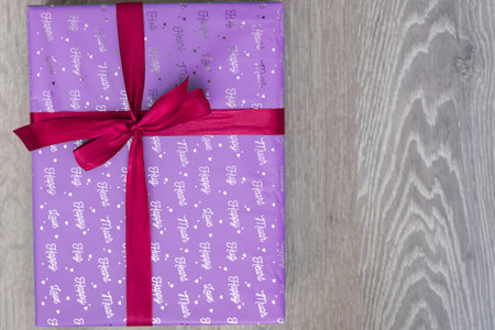 top view of purple violet color gift box with red ribbon bow on grey wooden background. Concept: holiday, celebration, birthday, New Year, Christmas, Valentines Day, Mothers Dayの写真素材