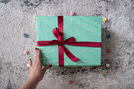 woman hand holding green turquoise color gift box with red ribbon bow on grey background. Concept: holiday, celebration, birthday, New Year, Christmas, Valentines Day, Mothers Day,の写真素材