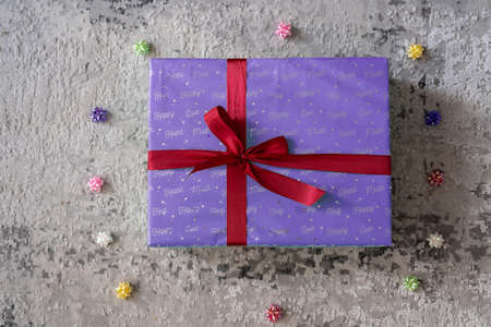 top view of purple violet color gift box with red ribbon bow on grey wooden background. Concept: holiday, celebration, birthday, New Year, Christmas, Valentines Day, Mothers Dayの写真素材