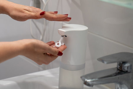 automatic sensor touchless soap dispenser, close up woman washing hands with soap and water, white foam, in the bathroom, under tap in the sink, personal hygiene and careの写真素材